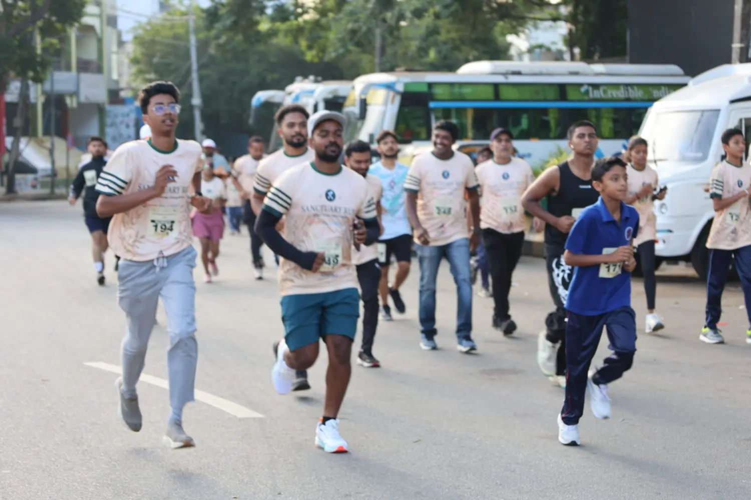 Runners of all ages in Sanctuary Run T-shirts and race bibs running along a city road